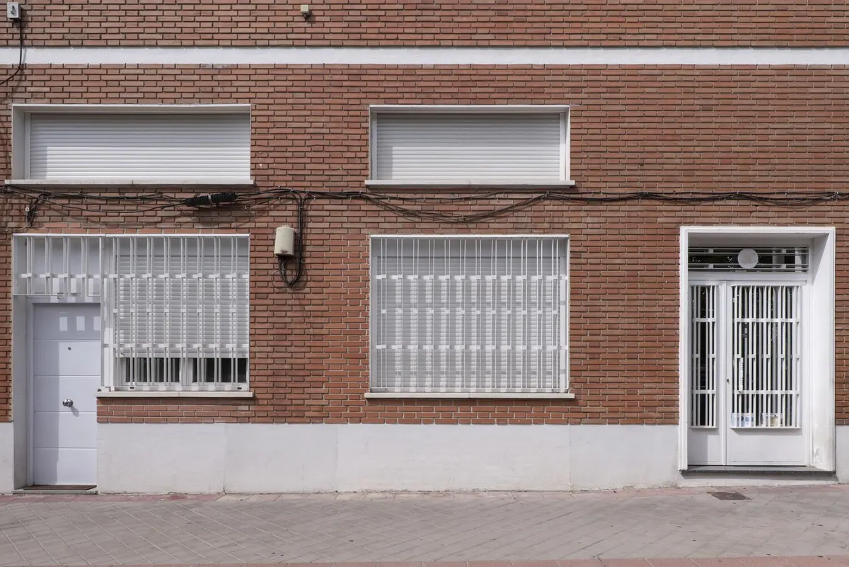 Façade de maison de ville en brique, volets roulants blancs baissés à l'étage et grilles au rez-de-chaussée
