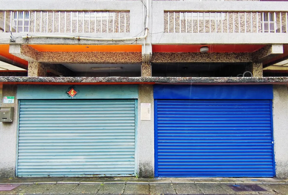 Deux rideaux métalliques de boutiques baissés, l'un bleu clair et l'autre bleu vif, au rez-de-chaussée d'un immeuble
