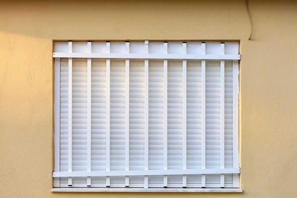 Volet roulant blanc entièrement baissé dans une fenêtre de façade enduite couleur sable